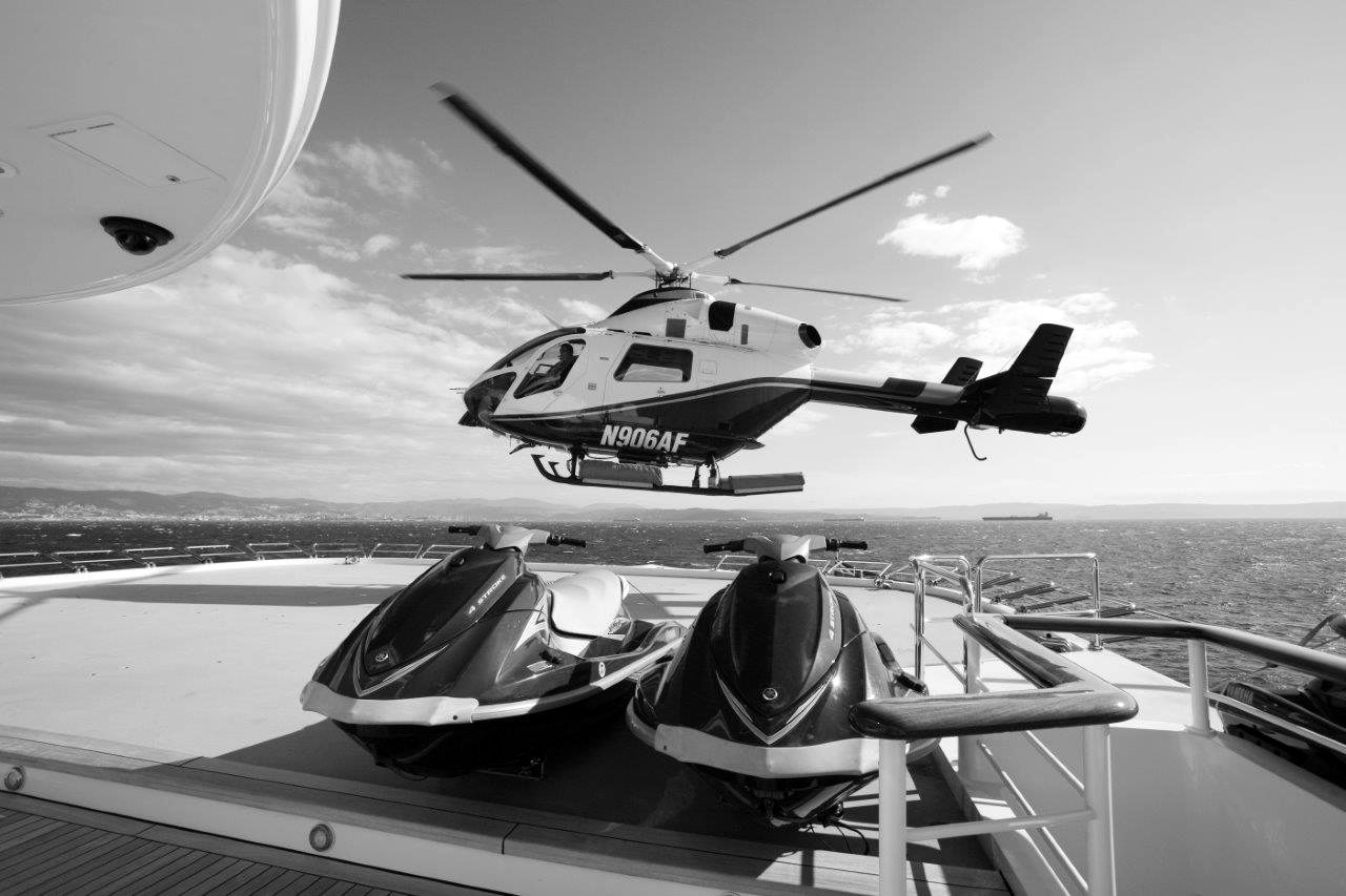 A helicopter above a superyacht helipad with jet skis on the foredeck