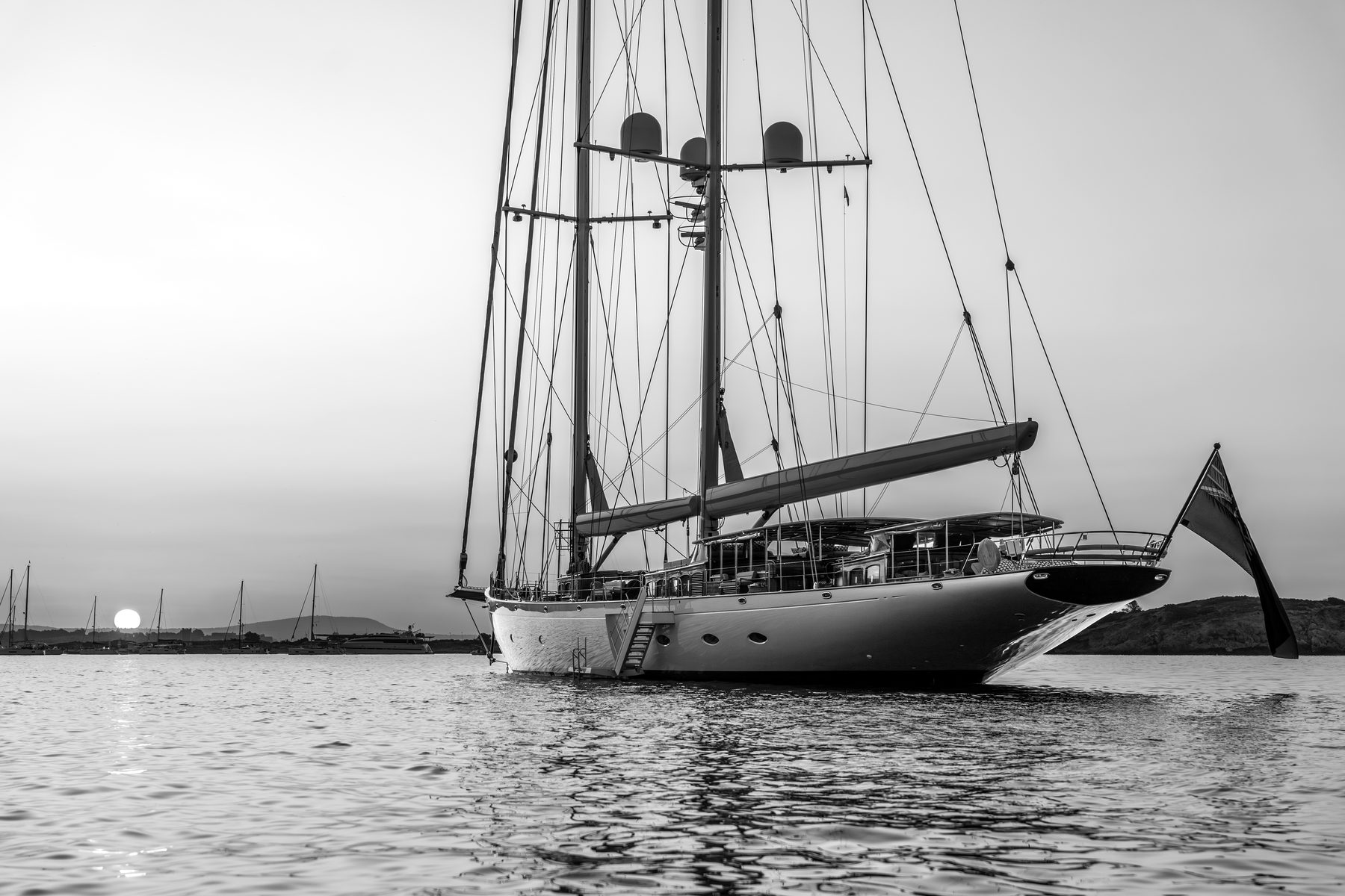 A large two-masted sailing yacht at anchor against a sunset