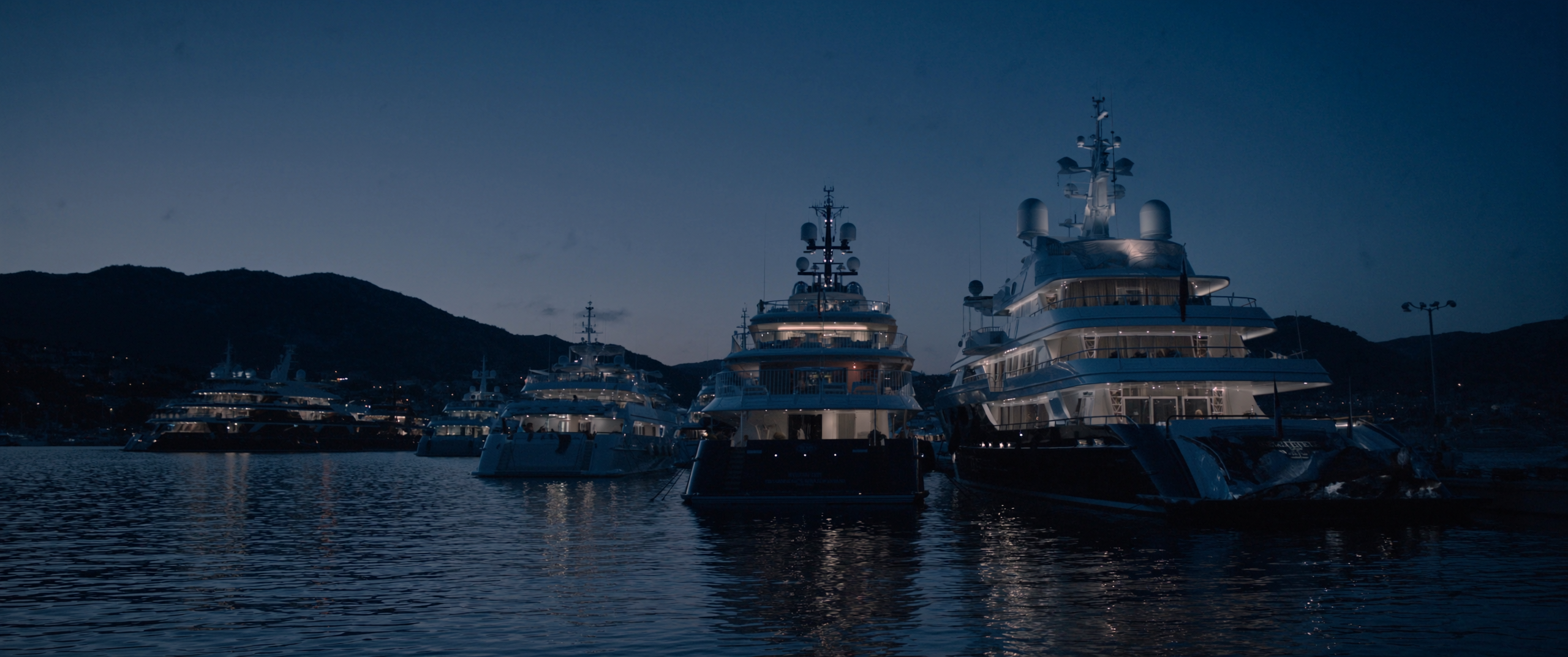 A quiet superyacht marina at blue hour, vessels lit against a deep twilight sky