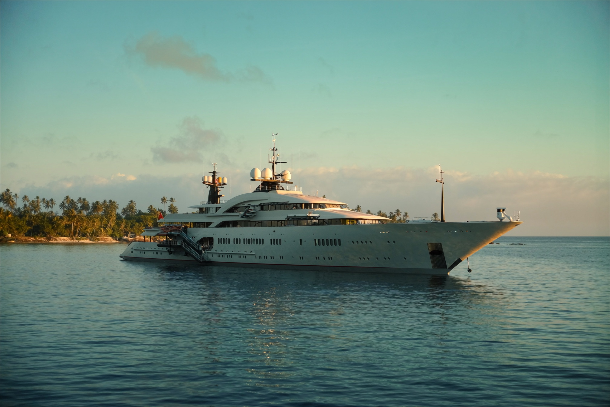 A superyacht anchored off a tropical island at sunset